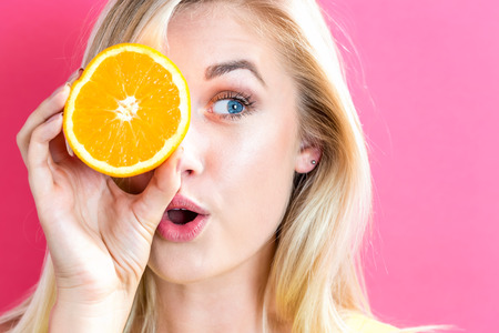 Happy young woman holding oranges halves on a pink backgroundの写真素材