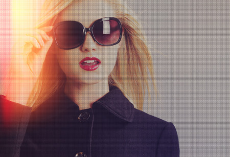 Beautiful young blonde woman in a black coat and sunglasses in led grid conceptの写真素材