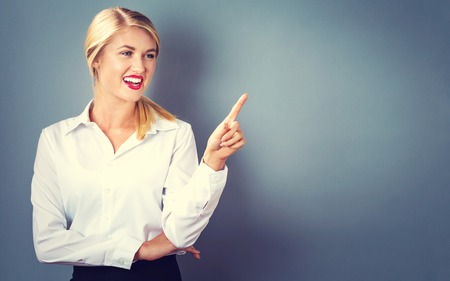 Young woman pointing something on a gray backgroundの写真素材