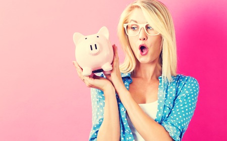 Young woman with a piggy bank on a pink backgroundの写真素材