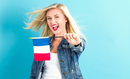 Happy young woman holding French flag on a blue backgroundの写真素材