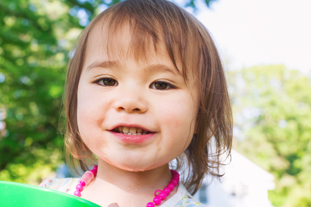 Happy toddler girl playing with watering cans and buckets outsideの写真素材