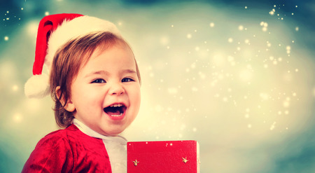 Happy Toddler girl wearing a Santa hat with a Christmas present boxの写真素材