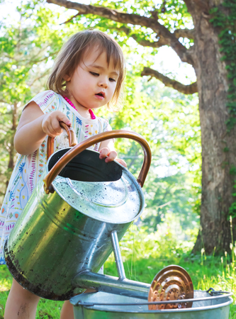 Happy toddler girl playing with watering cans and buckets outsideの写真素材