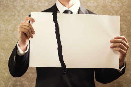Businessman holding a torn sign board on a dark backgroundの写真素材
