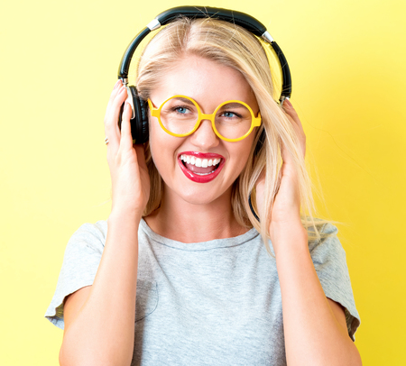 Happy young woman with headphones on a yellow backgroundの写真素材