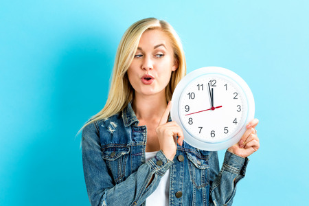 Young woman holding a clock showing nearly 12