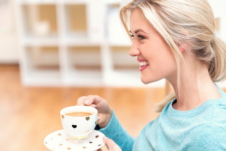 Happy young woman drinking coffee at homeの写真素材