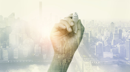 Double exposure of hand holding a pen and city backgroundの写真素材