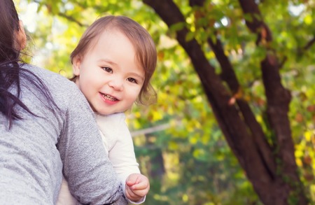 Happy toddler being carried by her mother outsideの写真素材