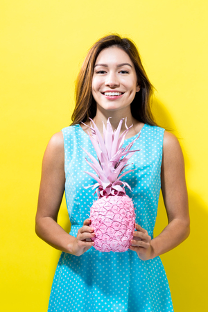 Happy young woman holding a pineapple on a yellow backgroundの写真素材