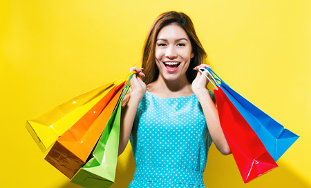 Happy young woman holding shopping bags on a yellow backgroundの写真素材
