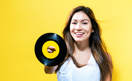 Happy young woman holding a record on a yellow backgroundの写真素材