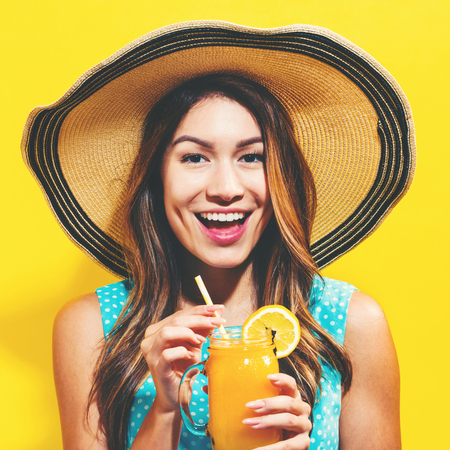 Happy young woman drinking smoothie on a yellow backgroundの写真素材