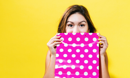 Happy young woman holding a shopping bag on a yellow backgroundの写真素材