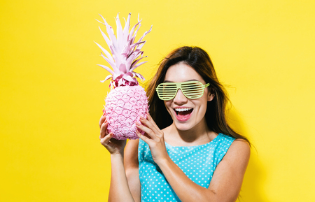 Happy young woman holding a pineapple on a yellow backgroundの写真素材