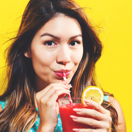 Happy young woman drinking smoothie on a yellow backgroundの写真素材
