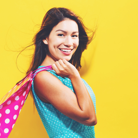 Happy young woman holding a shopping bag on a yellow backgroundの写真素材