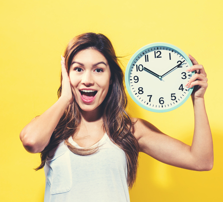 Young woman holding a clock on a yellow back groundの写真素材