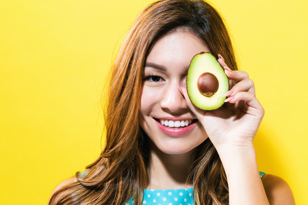 Happy young woman holding an avocado halve on a yellow background