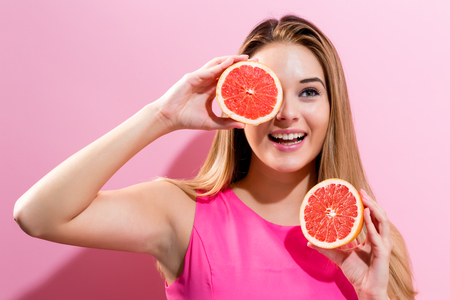 Happy young woman holding grapefruit halves on a pink backgroundの写真素材