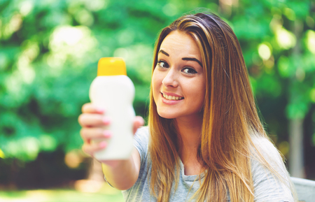Young woman a bottle of sunblock outside on a summer day