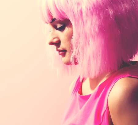 Beautiful woman in a bright pink wig on a pink backgroundの写真素材