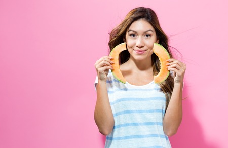 Happy young woman holding slices of cantaloupe on a pink backgroundの写真素材