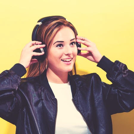 Happy young woman with headphones on a yellow backgroundの写真素材