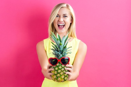 Happy young woman holding a pineapple on a pink backgroundの写真素材