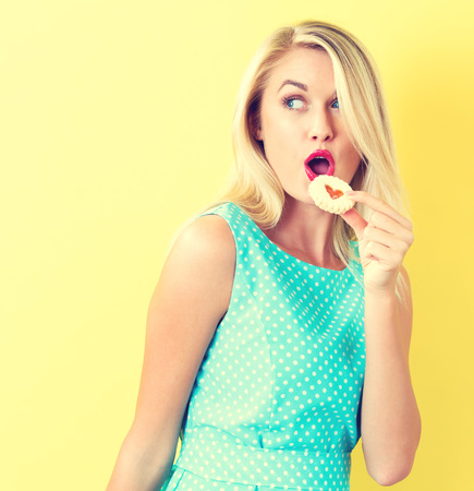Happy young woman with cookie on a yellow backgroundの写真素材