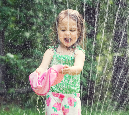Happy toddler girl playing in a sprinkler on a hot summer dayの写真素材