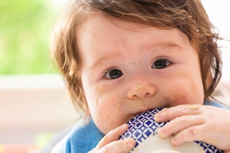 Happy little baby boy eating food from a bowlの写真素材
