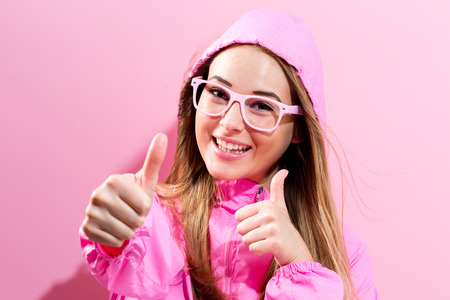 Happy young woman giving thumbs up on a pink backgroundの写真素材