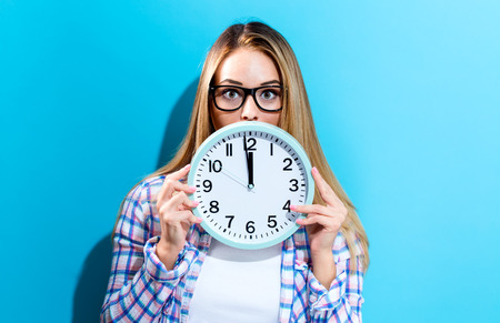 Young woman holding a clock showing nearly 12