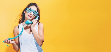 Young woman talking on old fashion phone on a yellow background