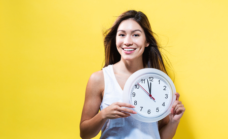 Young woman holding a clock showing nearly 12の写真素材