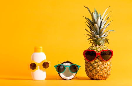 Pineapple, coconut and sunblock wearing sunglasses on a bright yellow backgroundの写真素材