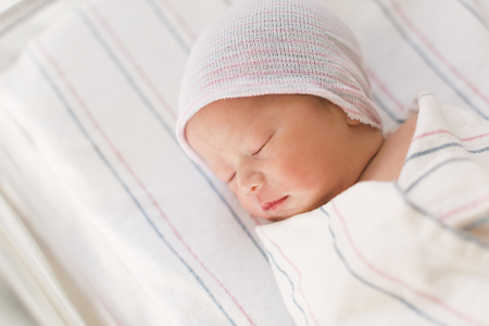 Newborn infant baby boy swaddled after birth lying in his hospital bedの写真素材