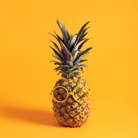Whole pineapple with glasses on a bright yellow backgroundの写真素材