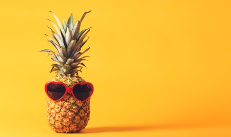 Whole pineapple with sunglasses on a bright yellow backgroundの写真素材