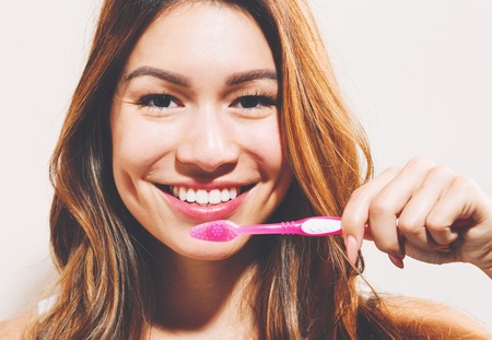 Happy woman holding a toothbrush on a off white backgroundの写真素材