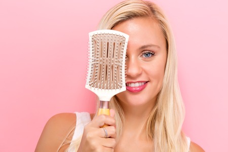 Beautiful woman holding a hairbrush on a pink backgroundの写真素材