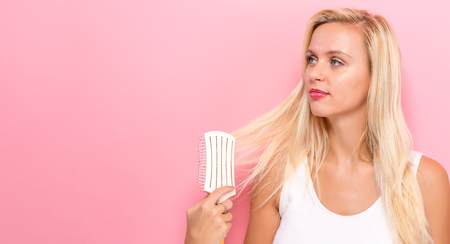 Beautiful woman holding a hairbrush on a pink backgroundの写真素材