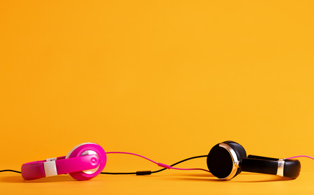 Pink and black headphones entwining their wires together on a yellow backgroundの写真素材