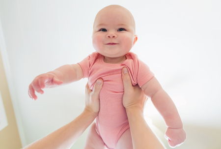 Happy infant baby girl being held up in the air by her parentの写真素材