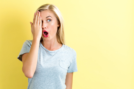 Happy young woman covering one eye with her hand on a bright yellow backgroundの写真素材