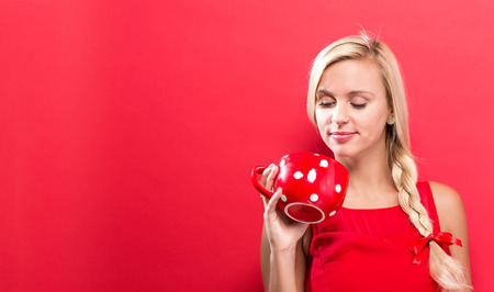 Happy young woman drinking coffee on a red backgroundの写真素材