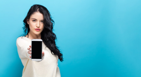 Young woman holding out a cellphone in her handの写真素材