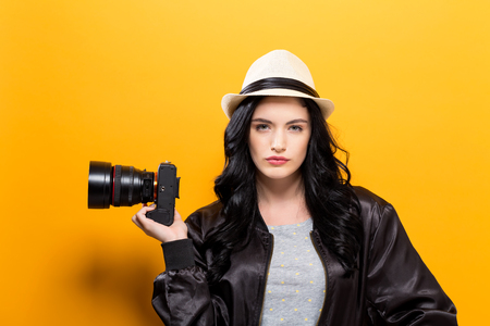 Young woman holding a camera on a yellow backgroundの写真素材